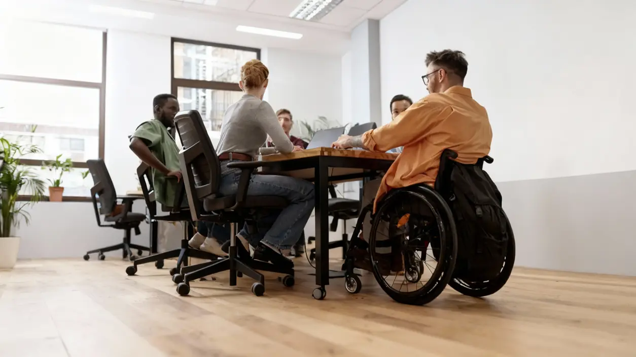Persone sedute attorno a un tavolo in ufficio, inclusa una persona in sedia a rotelle