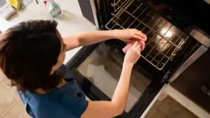 Persona che pulisce la griglia interna di un forno elettrico con un panno rosa