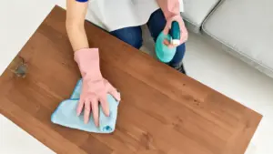Persona con guanti rosa pulisce un tavolo in legno con panno e spray