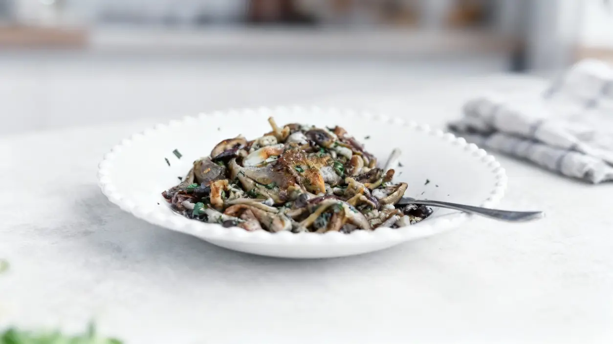 Piatto di funghi trifolati servito in una ciotola bianca con forchetta