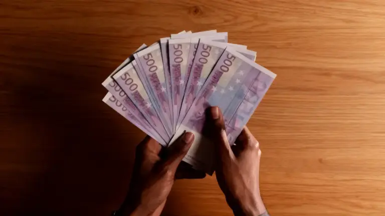 Una persona tiene in mano diverse banconote da 500 euro su un tavolo in legno
