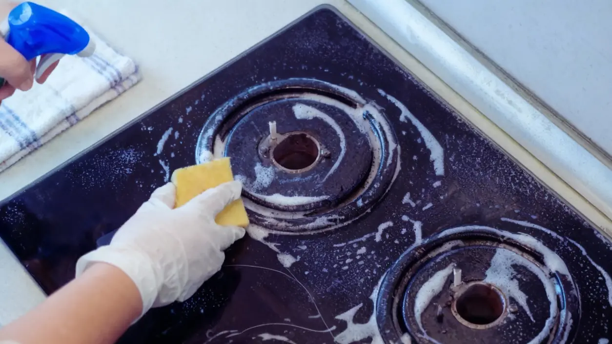 Pulizia di un piano cottura incrostato con una spugna e detergente